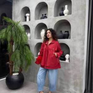 Vista frontal de chaqueta roja estilo anorak con bolsillos frontales y cremalleras laterales, combinada con jeans azul claro y zapatillas color camel. - Mayoreo Turquía