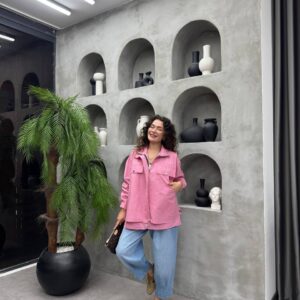 Modelo posando con chaqueta roja de corte relajado, con la mano en el bolsillo, superpuesta sobre una prenda interior más larga y pantalones de mezclilla. - Mayoreo Turquía