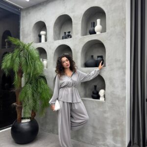 عارض يميل على حافة كونكريتية مرتدياً جاكيت فضي بسحاب وبنطال فضفاض مع خطوط بيضاء.