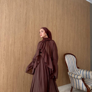 Standing view of brown ruffled gown with cascading tiers, billowy sleeves and belted waist, paired with a matching hijab.