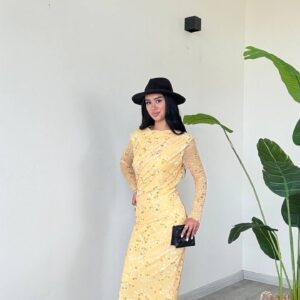 Three-quarter view of yellow midi dress showing draped waist, sheer dotted sleeves and a black clutch.