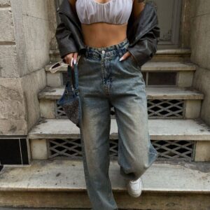 Close-up of ruffled light grey bandeau, leather jacket draped, faded high-waist jeans and white sneakers. available for wholesale in Turkey.