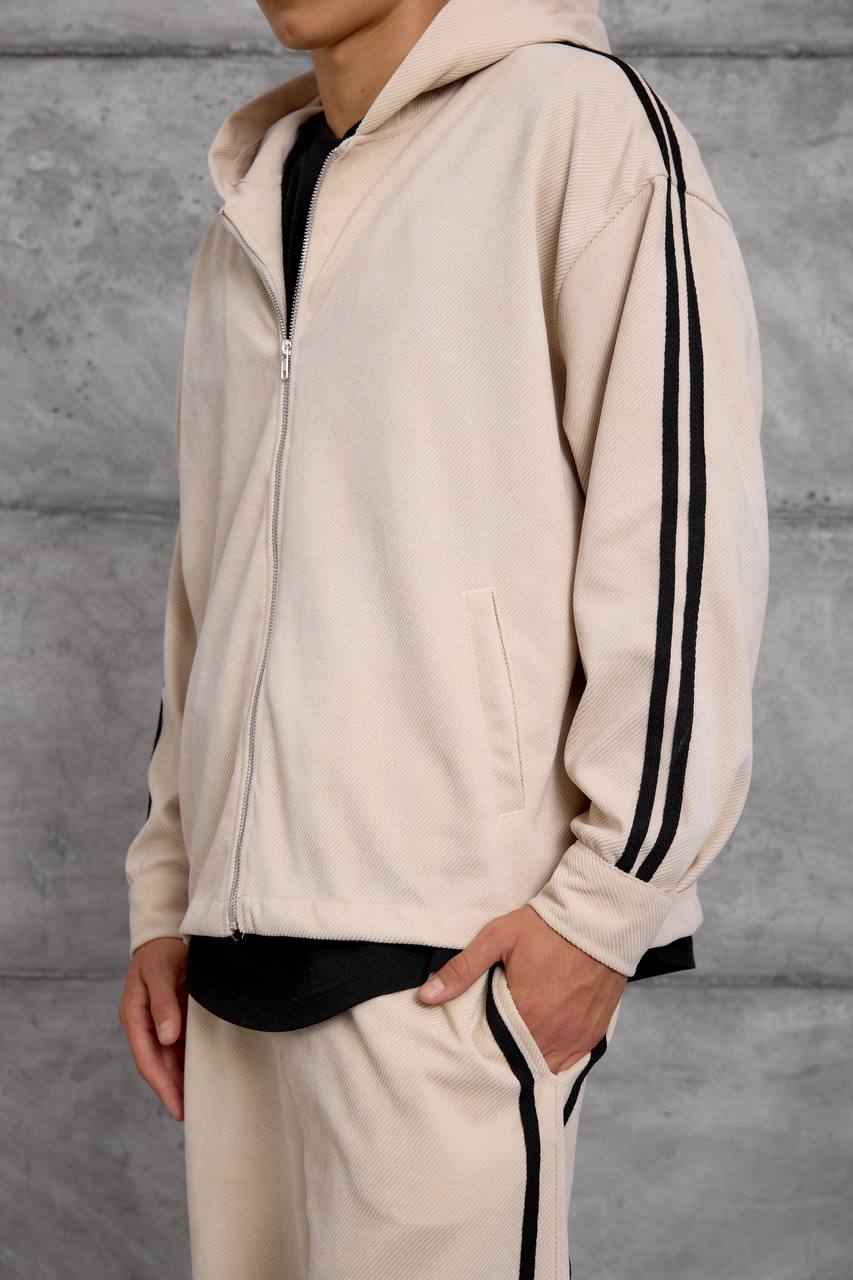 beige-hoodie-stripe-detail-1639 Close view of a beige hooded jacket showing its silver zipper, front pocket, and double black sleeve stripes.