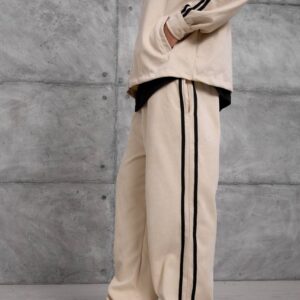 Side view of loose beige track pants with two black stripes running down the leg.