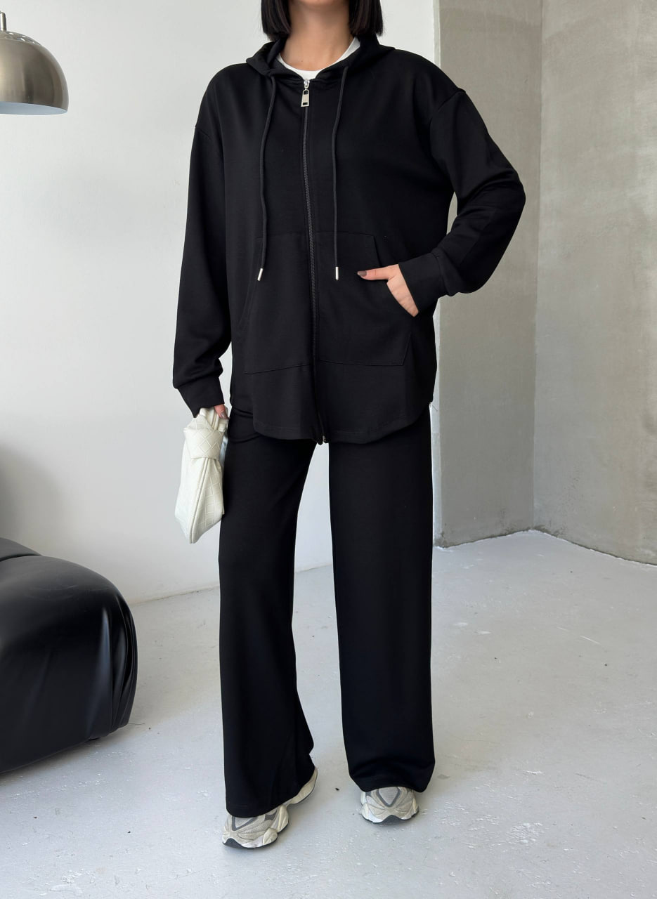 conjunto-capucha-negro-frente-9263-turquia-mayorista Vista frontal de una sudadera con capucha negra con cremallera completa y bolsillos frontales, combinada con pantalón ancho.