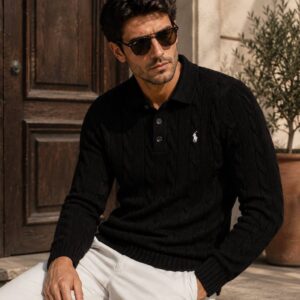 Man wearing a black long-sleeve cable-knit polo sweater with a button placket and small light-colored chest emblem.