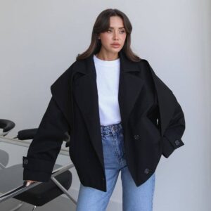 Frau trägt eine oversized schwarze Jacke mit breiten Revers, geknöpften Ärmelabschlüssen und hüftkurzem Saum. - Großhandel Türkei