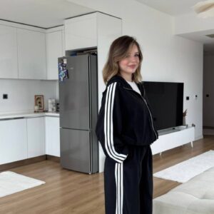 Side view of a black hooded zip-up jacket and matching wide-leg pants with three white stripes.