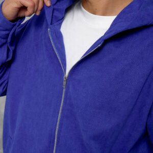 Close-up showing the blue jacket's textured fabric, silver zipper, and hood over a white shirt.