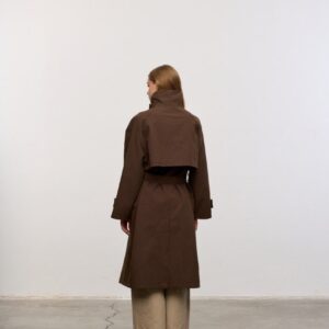 Rear view of brown mid-length coat with cropped cape yoke, belted waist and high collar over trousers.