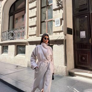 Modell geht in braunem Trenchcoat, Hände in Taschen, sichtbare Metallknopf-Details an den Manschetten und entspannte Silhouette - Großhandel Türkei.