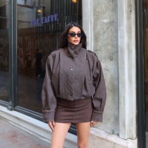 Brown denim jacket shown from the front with a raised collar, metal snaps, and roomy sleeves.