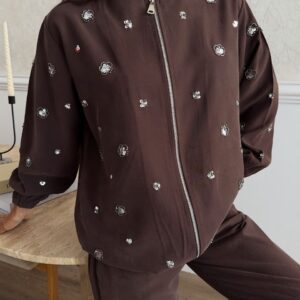 Close-up of a brown jacket with a silver front zipper, gathered cuffs, and scattered floral embellishments