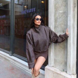 Model stands in a brown button-front jacket and matching short skirt with contrast seam details.