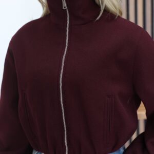 Close view of the burgundy jacket's high collar, silver zipper, smooth fabric, and two narrow front pockets.
