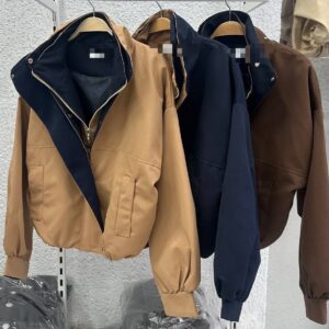 Several cropped jackets hang on a rack in tan, navy, and brown, featuring contrast hoods and front pockets.