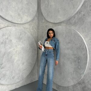 Modelo apoyado en una esquina con chaqueta denim azul claro recortada, top corto blanco y jeans de tiro alto. Disponible al por mayor en Turquía. - Mayorista en Turquía