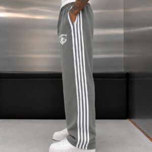 Side view showing gray joggers with three white stripes, a side pocket, and a gathered elastic waist.
