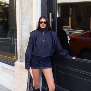 Model poses in a dark indigo jacket featuring a tall collar, snap buttons, and voluminous sleeves.