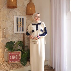 Front view of ivory knit maxi with navy collar, pocket flaps, striped cuff accents, model holding small handbag.