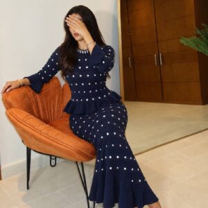 Seated model wearing navy knit peplum dress with horizontal pearl studs and flared hem available for wholesale in Turkey.