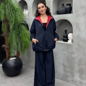 Marineblaue Reißverschlussjacke mit rotem Innenkragen kombiniert mit marineblauer Weite-Hose, Frontansicht, Hände in den Taschen.