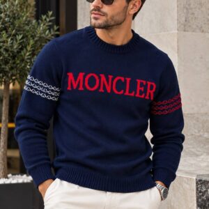 Model wearing a navy crewneck sweater with red chest lettering and contrasting patterned bands on the sleeves.