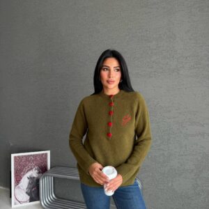 Olivgrüner weicher Strickpullover mit sechs auffälligen roten bedeckten Knöpfen vorne und dezentem Brustmonogramm.