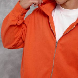 Close view of the orange hoodie's textured fabric, hood seam, and silver front zipper.