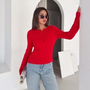 Model wearing a fitted red ribbed long-sleeve top with decorative front buttons and light-wash jeans, posed by a white archway. available for wholesale in Turkey.
