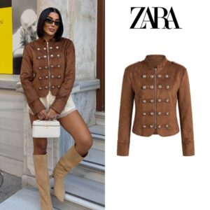Model steht auf Marmortreppen, trägt braune Wildleder-Militärjacke mit silbernen Verzierungen, cremefarbene Shorts und braune Stiefel, während sie eine weiße Handtasche hält. - Großhandel Türkei