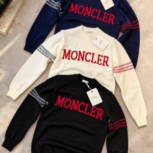 Navy, ivory, and black crewneck sweaters arranged together, each with red chest lettering and patterned sleeve bands.
