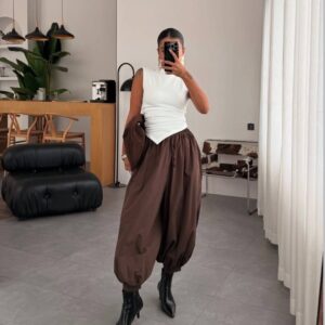 Full-length mirror selfie of white sleeveless asymmetric top paired with brown gathered harem pants and pointed black ankle boots.