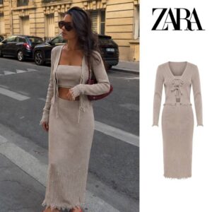 Beige two-piece knit set featuring a tie-front cardigan, fitted long skirt, pearl-like embellishments, and fringed hems.