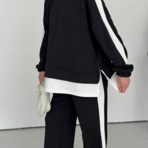 Close view of a black sweatshirt with elastic cuffs, white shoulder stripes, a layered hem, and matching striped pants.