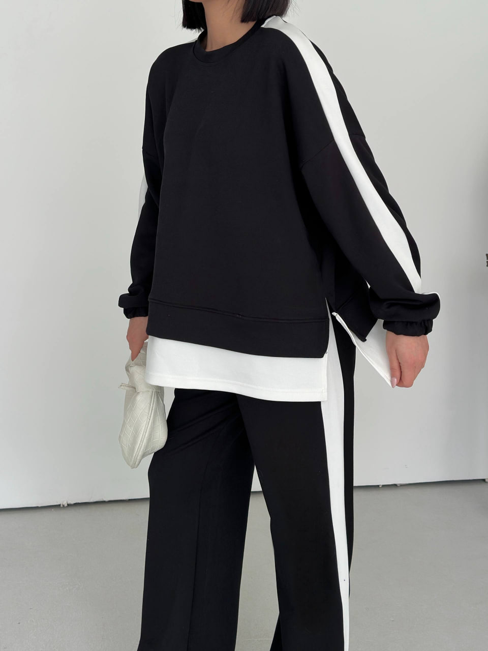 black-tracksuit-closeup-9172 Close view of a black sweatshirt with elastic cuffs, white shoulder stripes, a layered hem, and matching striped pants.