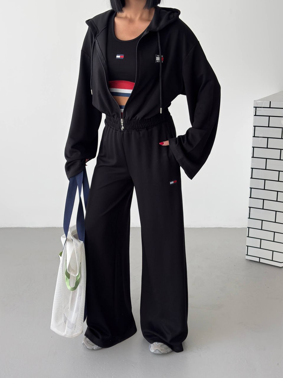 black-tracksuit-front-detail-8642 Black zip-front hoodie with drawstrings, matching wide-leg trousers, and a sleeveless top with striped accents.