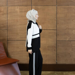 Side view of a black zip jacket with cream panels and matching pants with twin side stripes.