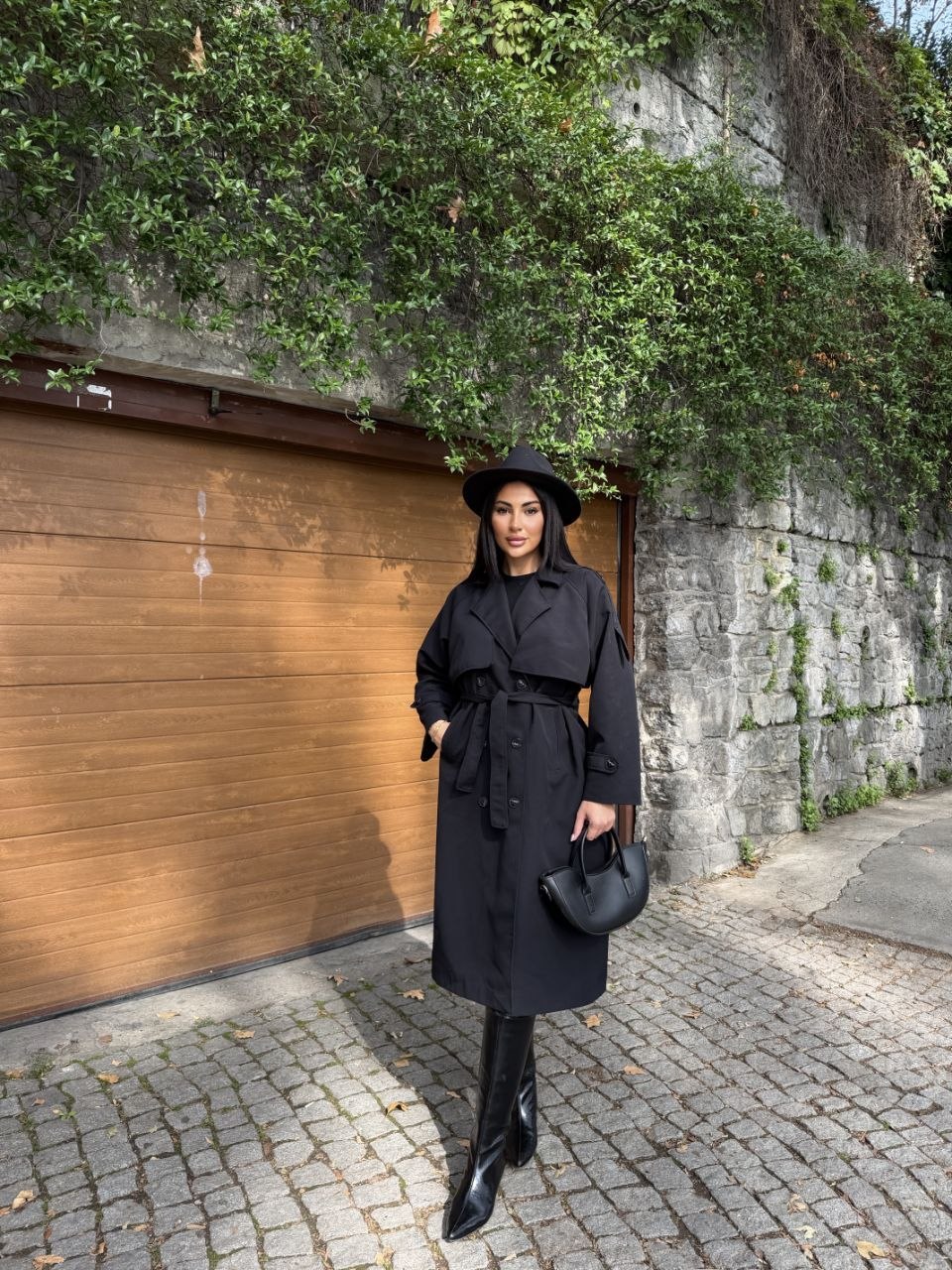 black-trench-belted-look-2946 Long black double-breasted trench coat with broad lapels, a tied waist belt, and buttoned cuff straps.