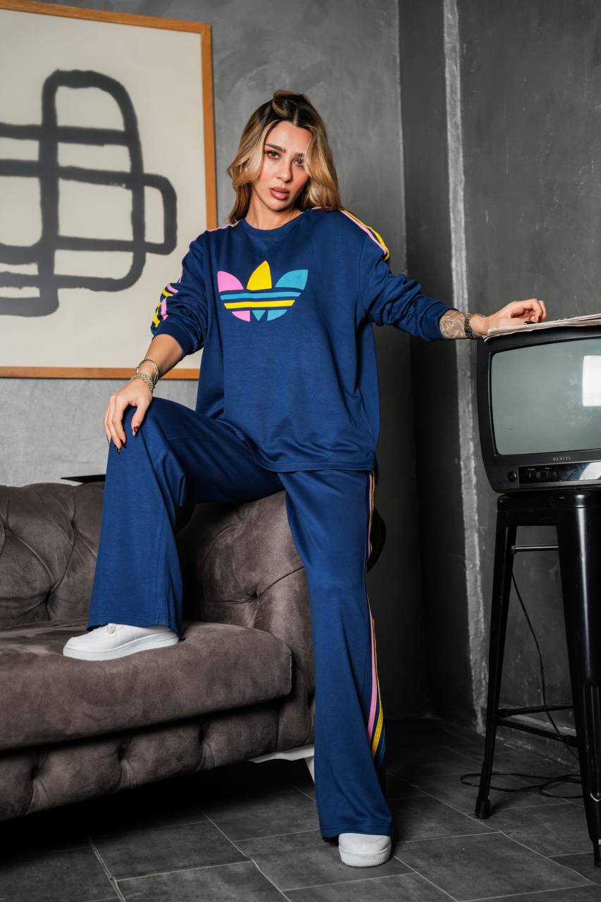 blue-tracksuit-seated-1629 Model wearing a blue sweatshirt and wide-leg pants with colorful sleeve and trouser stripes while seated.