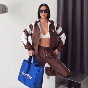 Brown zip jacket with white shoulder and sleeve panels, worn open over a white top with matching striped trousers.
