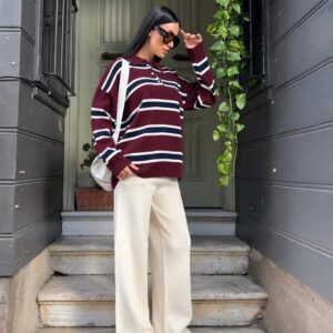 Angled view showing the sweater's burgundy ribbed cuffs, buttoned polo neckline, and horizontal navy and white stripes.