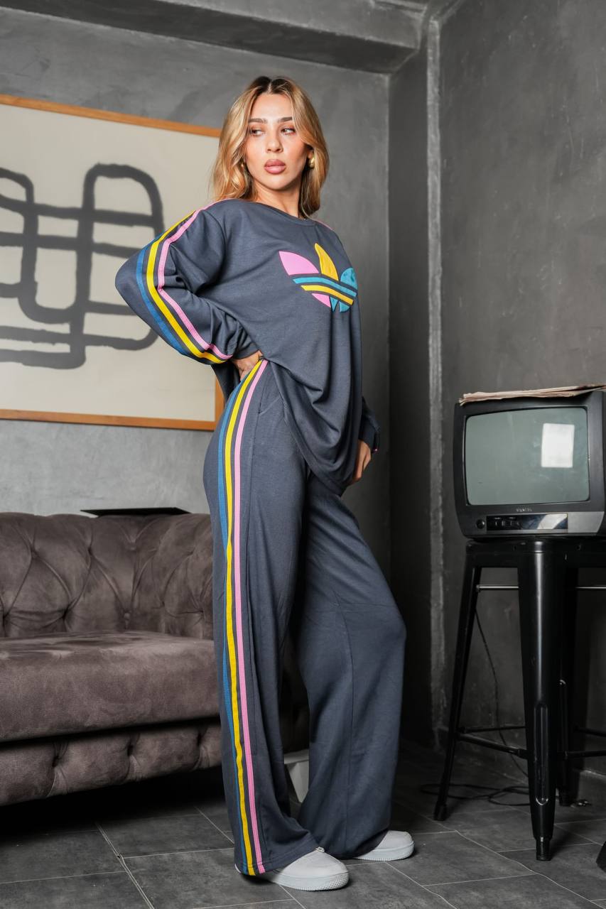charcoal-tracksuit-side-9163 Angled full-length view of a charcoal lounge set with loose pants and multicolor stripes along the sleeves and legs.