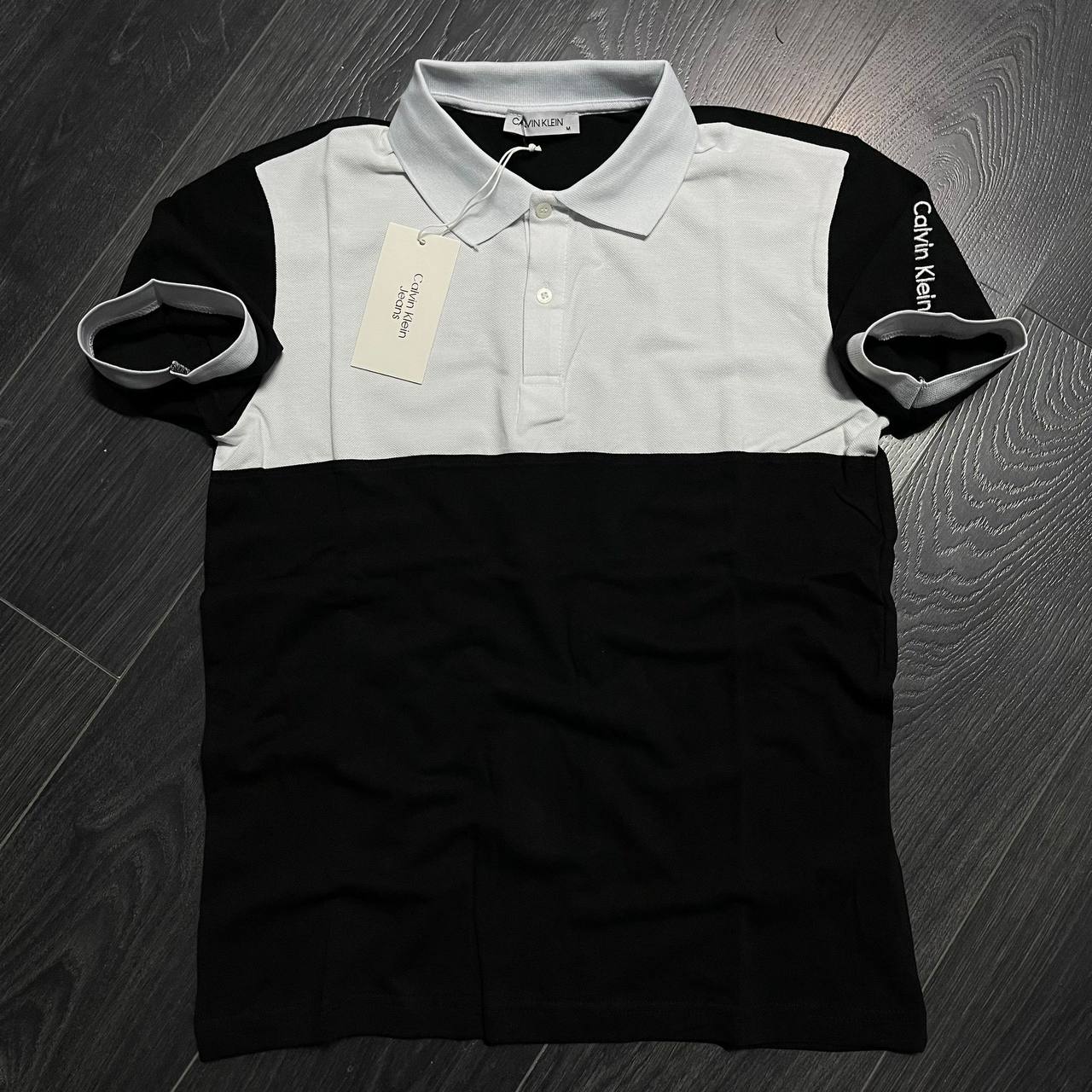 polo-color-block-disposicion-plana-6384 - Mayorista Turquía Plano cenital de un polo negro con panel blanco en el pecho, cuello de contraste y mangas cortas. Disponible para venta al por mayor en Turquía - Mayorista Turquía