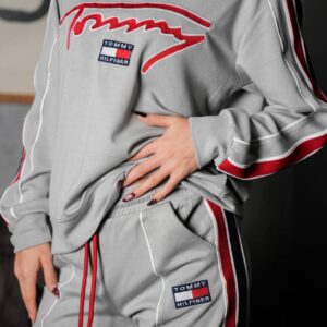 Close view of a light gray sweatshirt featuring a red-and-white chest graphic, striped sleeve trim, and matching pants.