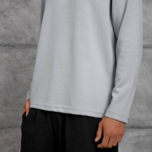 Close view of the light grey shirt's smooth fabric, straight hem, and stitched sleeve cuff.
