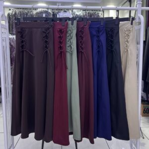 A rack displays long skirts in dark brown, burgundy, sage, plum, blue, navy, and beige, each with side lacing.