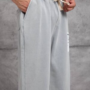 Front detail of light gray sweatpants with an elastic waistband, cream drawstring, and angled pockets.
