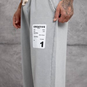 Close-up of a white rectangular graphic patch on light gray sweatpants beside a slanted pocket.
