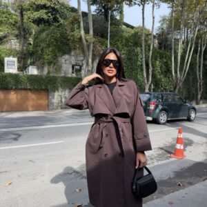 Woman wearing a long mauve trench coat with wide lapels, black buttons, cuff straps, and a tied belt. available for wholesale in Turkey.